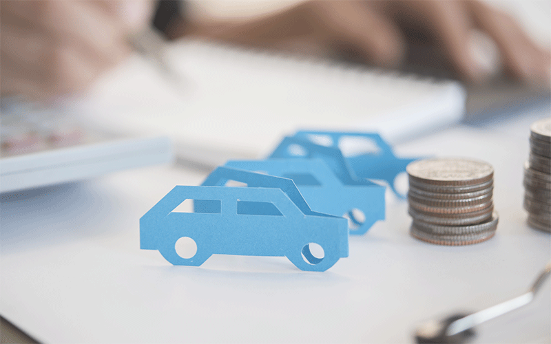 計算中の人の脇にコインと紙でつくった車が置かれている